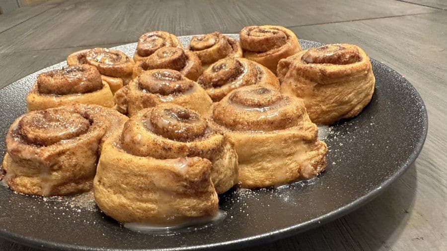 Air fryer cinnamon rolls dusted with cinnamon sugar arranged on a dark gray plate.