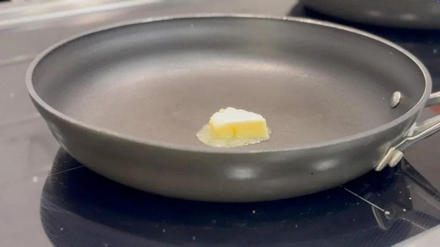 Melting butter in a gray nonstick skillet on a stovetop for cooking eggs.