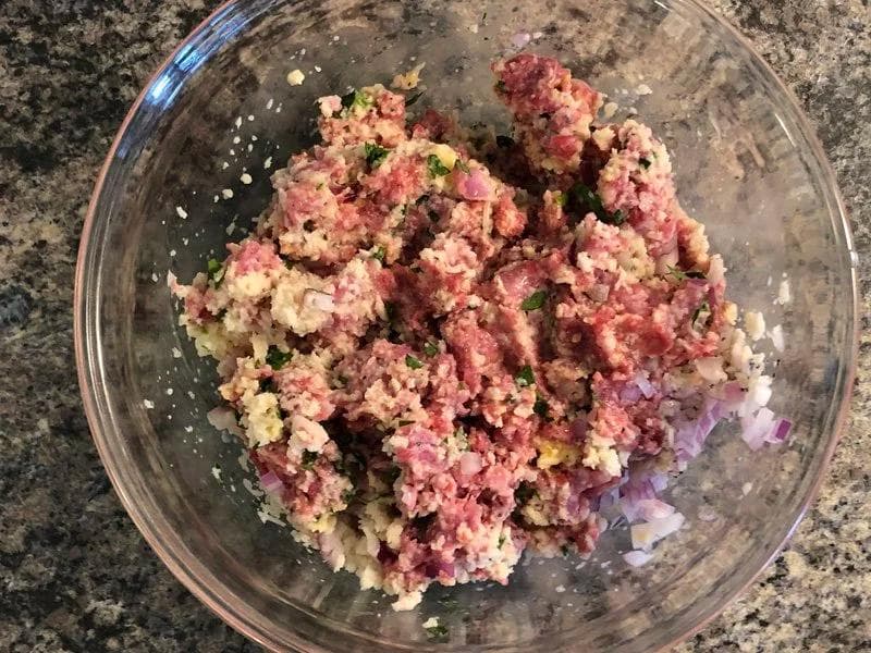 Raw meatball mixture with ground beef, pork, breadcrumbs, and herbs in a glass bowl before forming into balls.