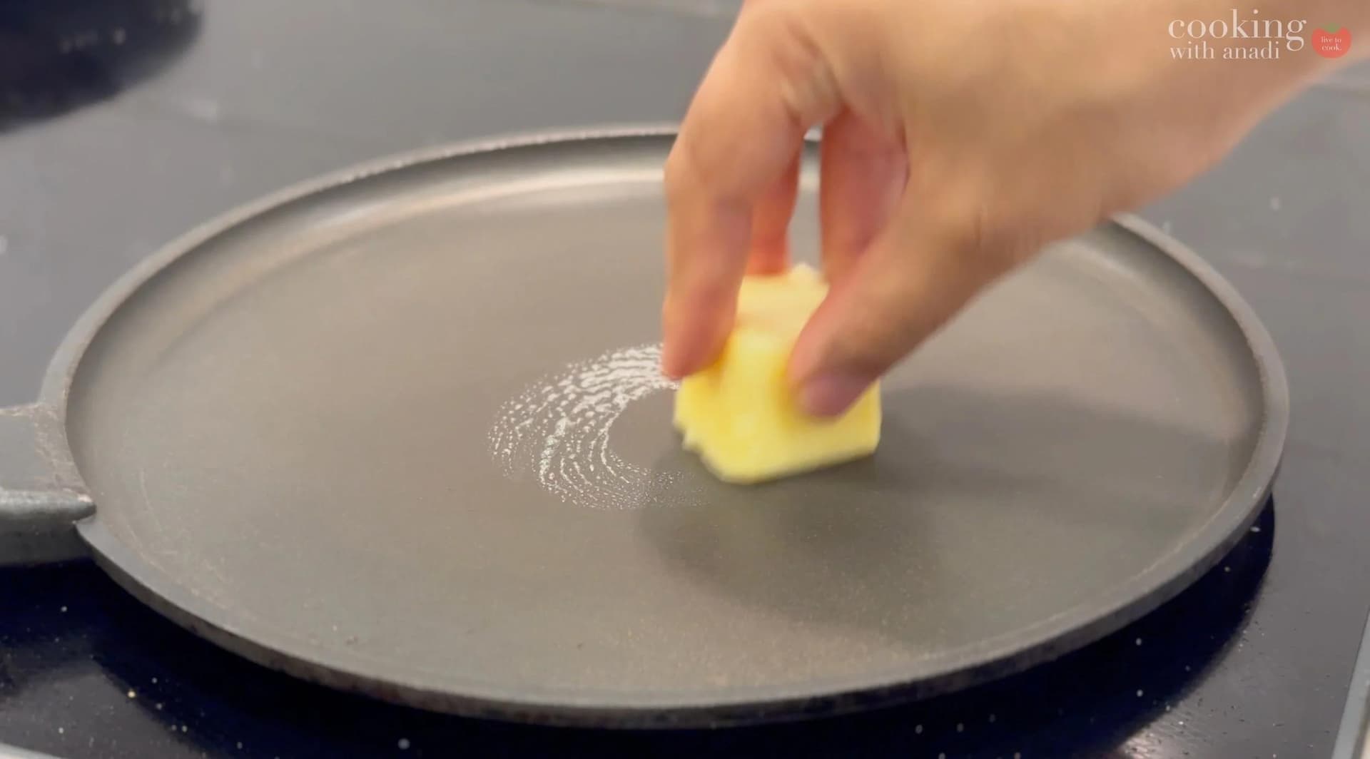 Buttering a griddle with a yellow butter square for toasting a patty melt sandwich.