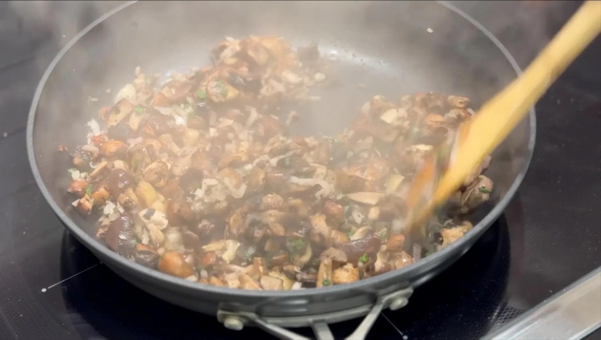 Sautéed mixed mushrooms with shallots and garlic being stirred in a pan with a wooden spoon.