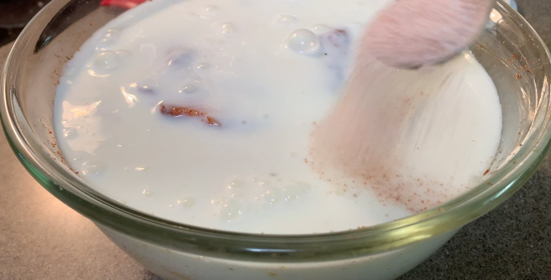 Raw chicken pieces marinating in buttermilk with salt in a glass bowl.