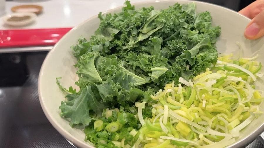 White bowl containing sautéed kale and zucchini noodles with green onions and chives for twice baked potato filling.