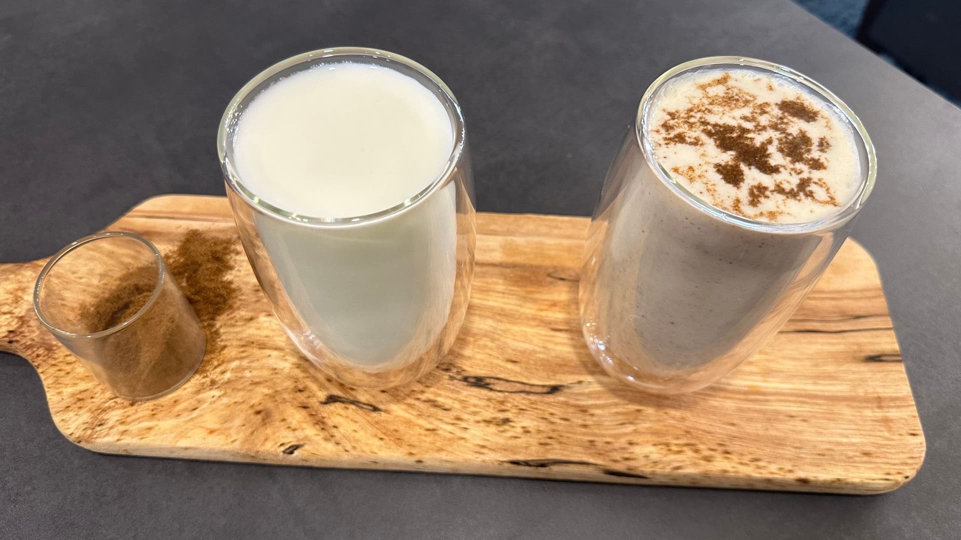 Two glasses of mattha on a wooden board: plain yogurt drink on left, spiced version with cinnamon on right.