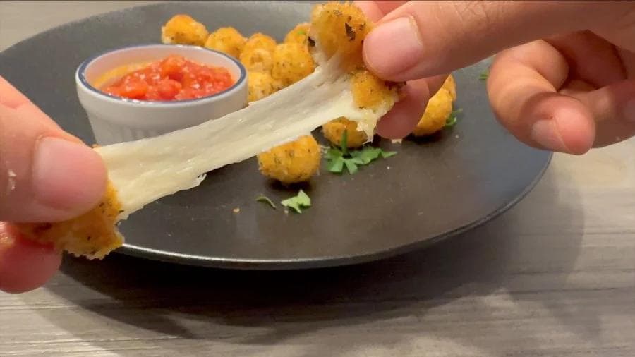Crispy golden fried mozzarella ball being pulled apart to show melted cheese stretch, served with marinara sauce for dipping.