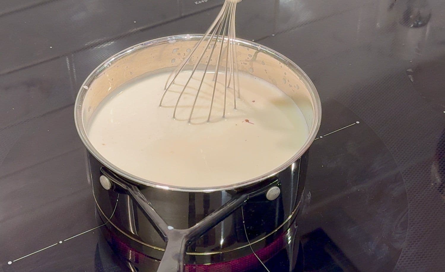 Nutella whisked into milk in a saucepan, creating a smooth, creamy chocolate mixture with a whisk resting in the pan.