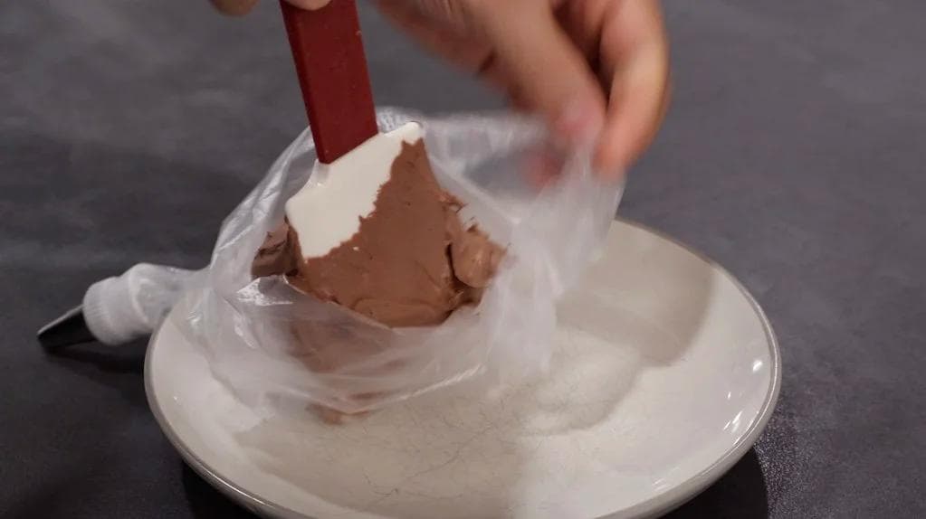 Whipped cream being piped from a bag onto a plate, showing soft peaks texture for Baileys hot chocolate topping.