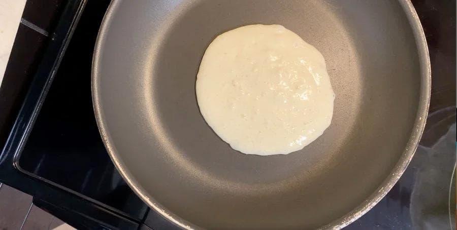 One buttermilk pancake cooking in a non-stick pan, showing bubbles forming on the surface.