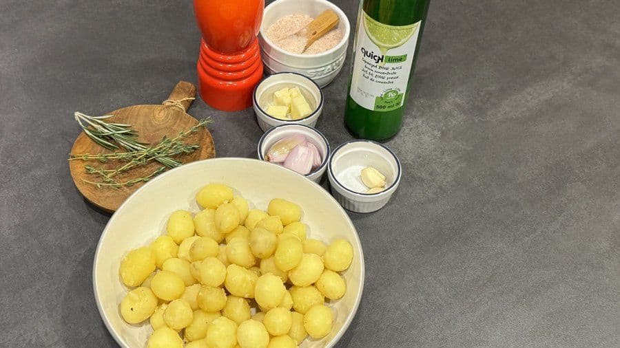 Raw Yukon gold baby potatoes in a white bowl with butter, garlic, shallots, and fresh rosemary ingredients displayed.