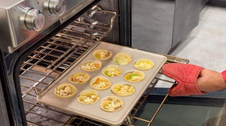 Muffin tin of baked egg cups being removed from oven, person wearing red sleeve holding tray.
