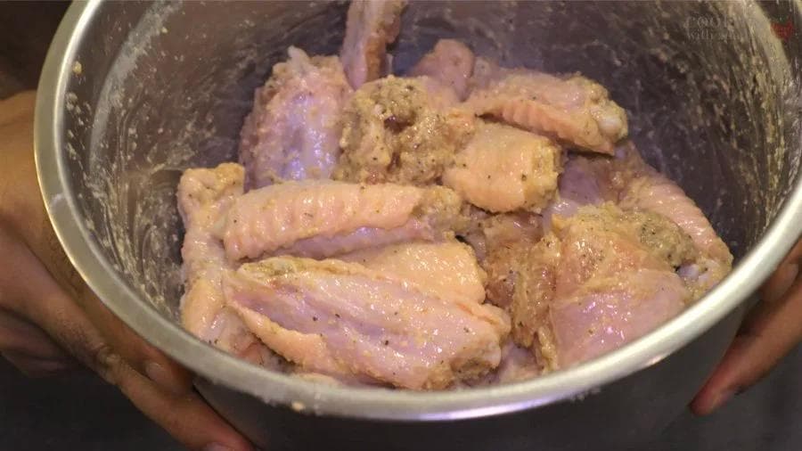 Seasoned raw chicken wings coated with spices and cornstarch in a mixing bowl.