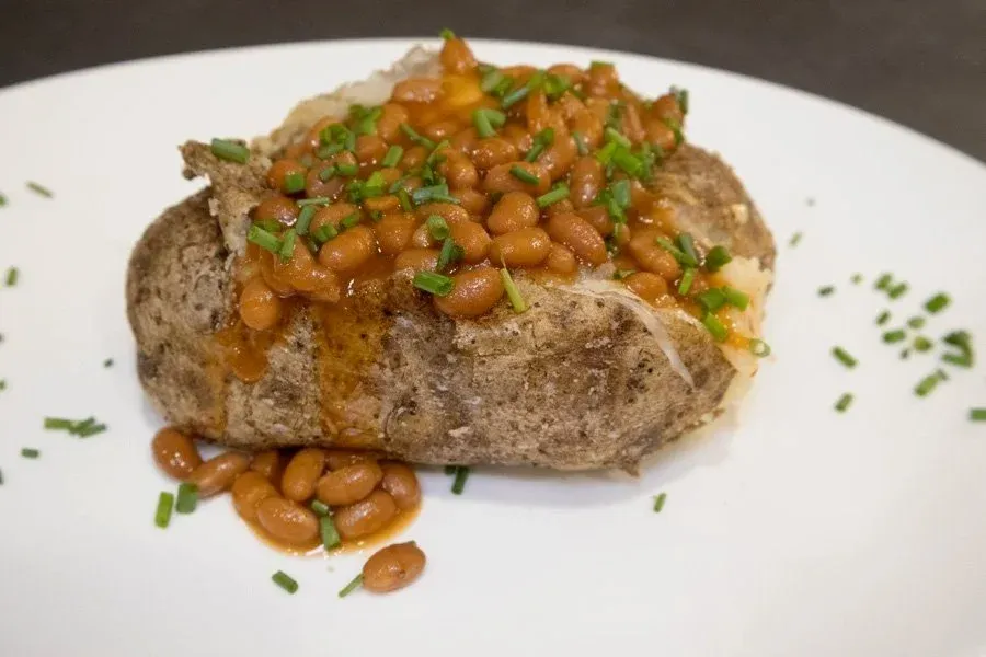 Baked jacket potato topped with baked beans and chopped chives on a white plate.