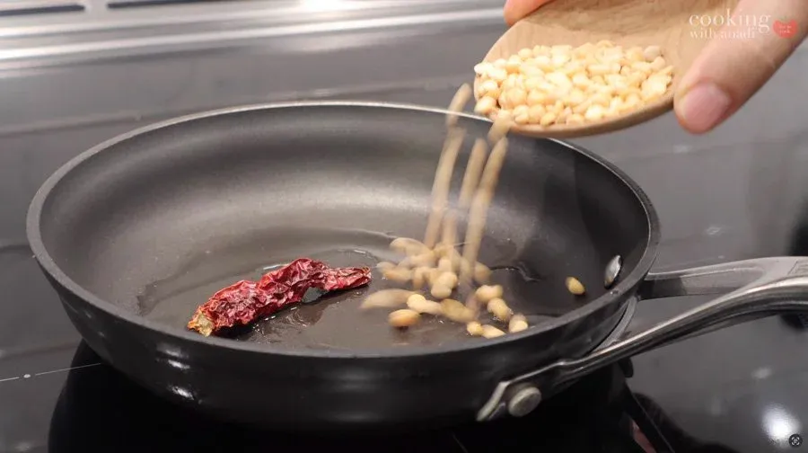 Pouring roasted chana dal into a pan with dried red chilies and coconut oil for tempering.