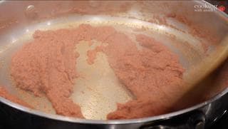 Red dal mixture simmering in a pan with tomato paste added to the center, ready to be stirred in.