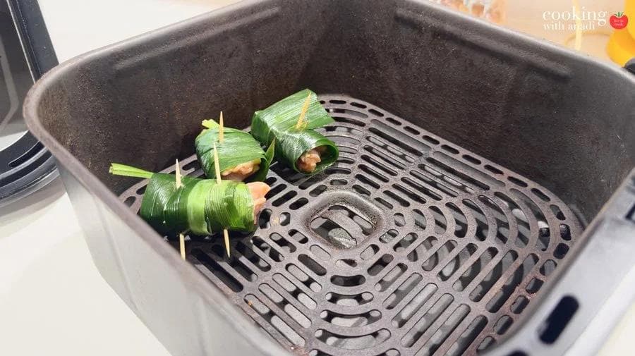 Pandan-wrapped chicken parcels secured with toothpicks arranged in a single layer in an air fryer basket.