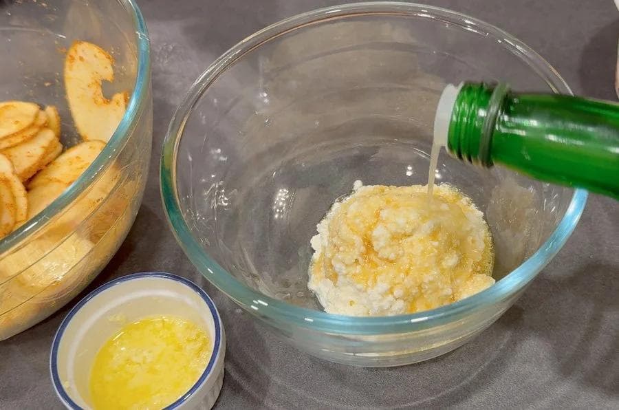 Ricotta mixture being poured into a glass bowl with melted butter drizzling from a green bottle.
