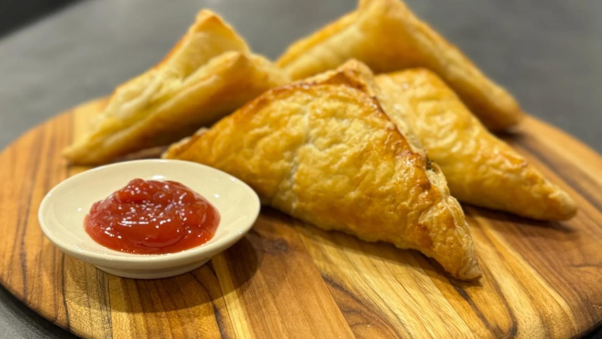 Golden baked mushroom puff pastry patties served with red chutney on a wooden board.