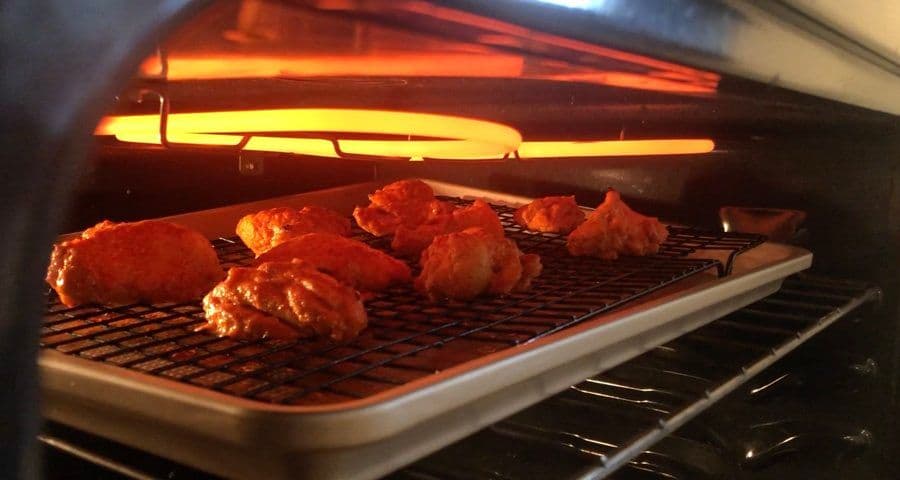 Marinated chicken tikka pieces broiling on a wire rack under the oven's heating element.