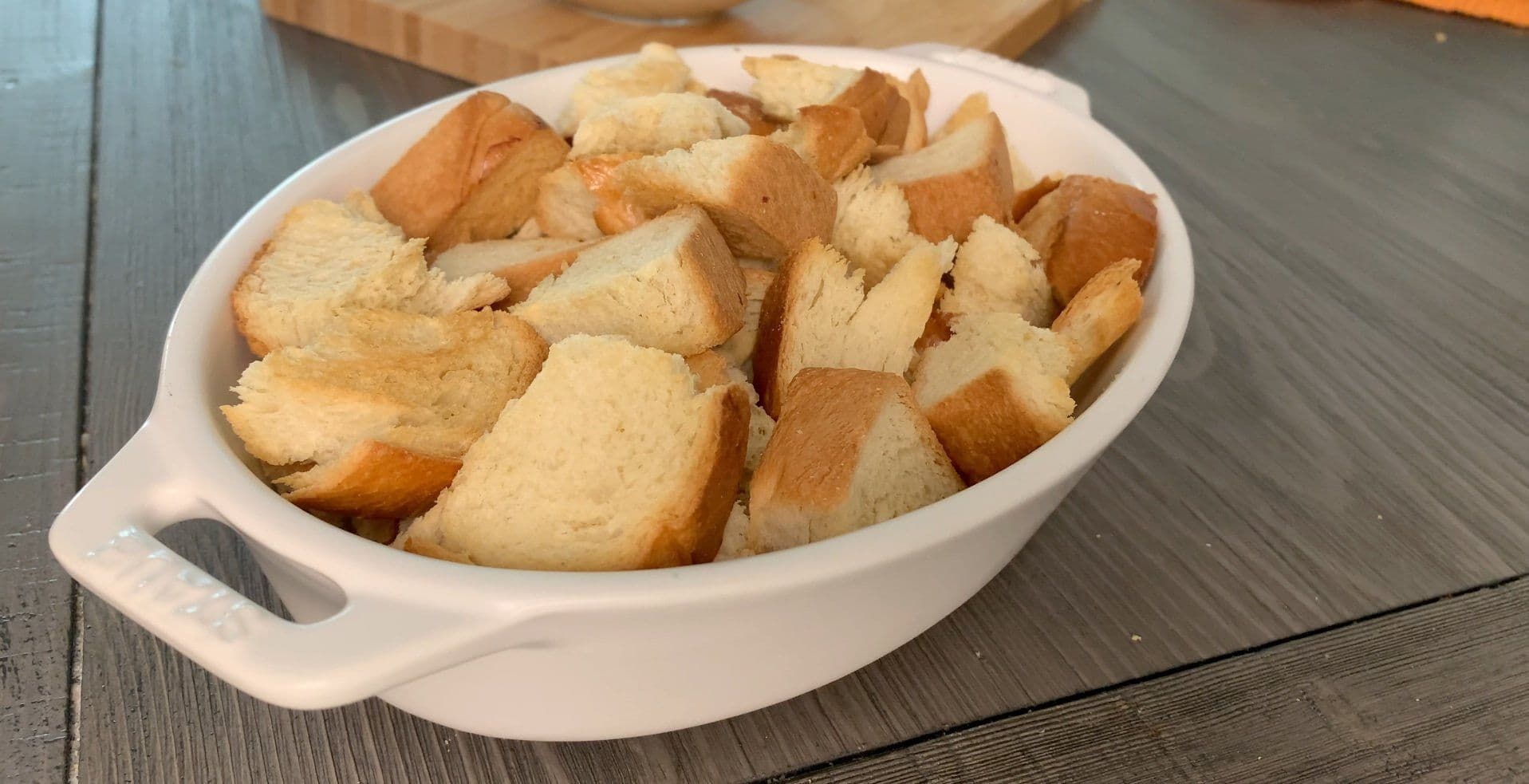 Cubed brioche bread pieces in a white oval baking dish, ready for custard mixture.