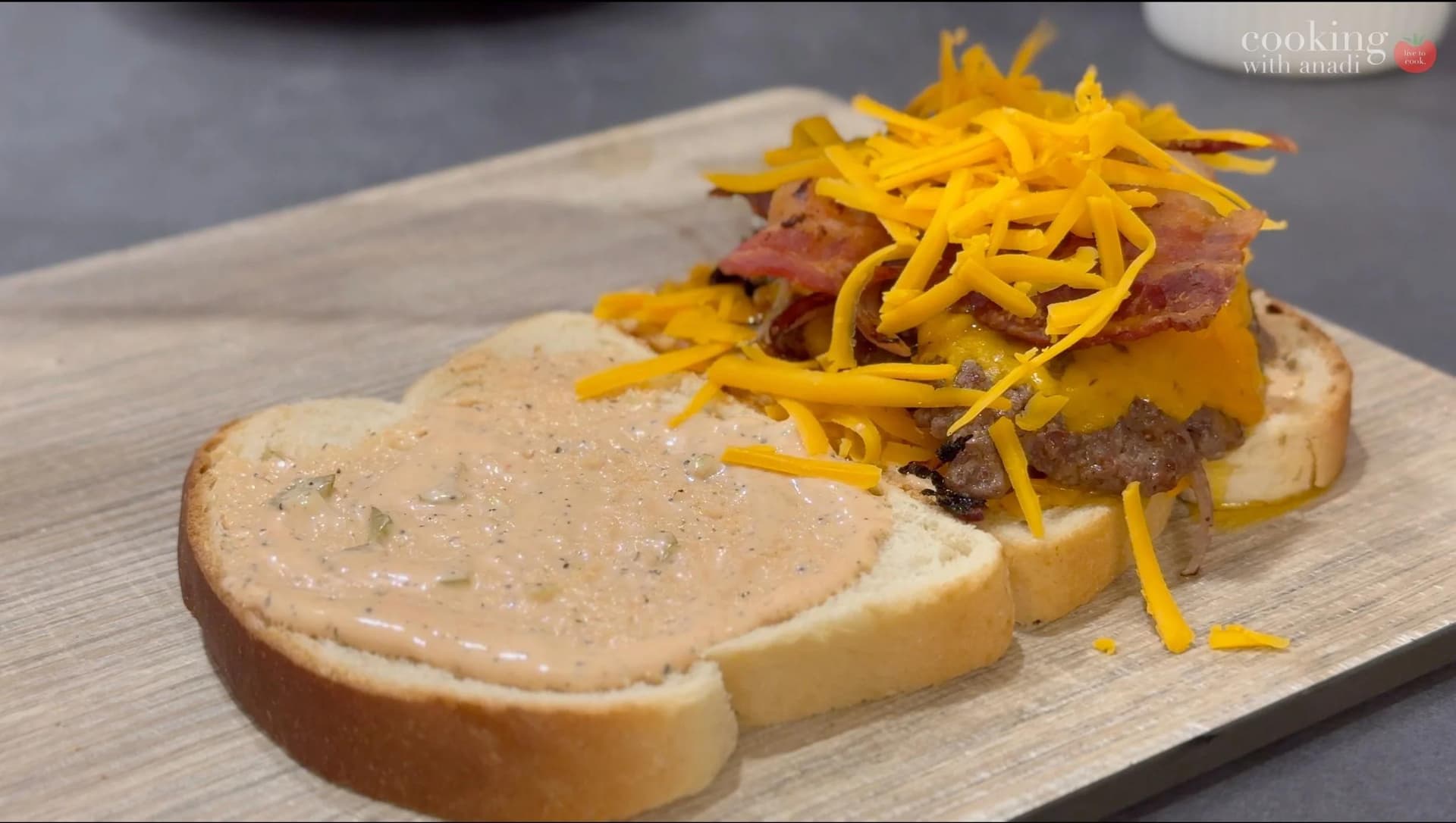 Smash burger patty melt with melted cheddar cheese, crispy bacon, and shredded cheddar on toasted bread with sauce.