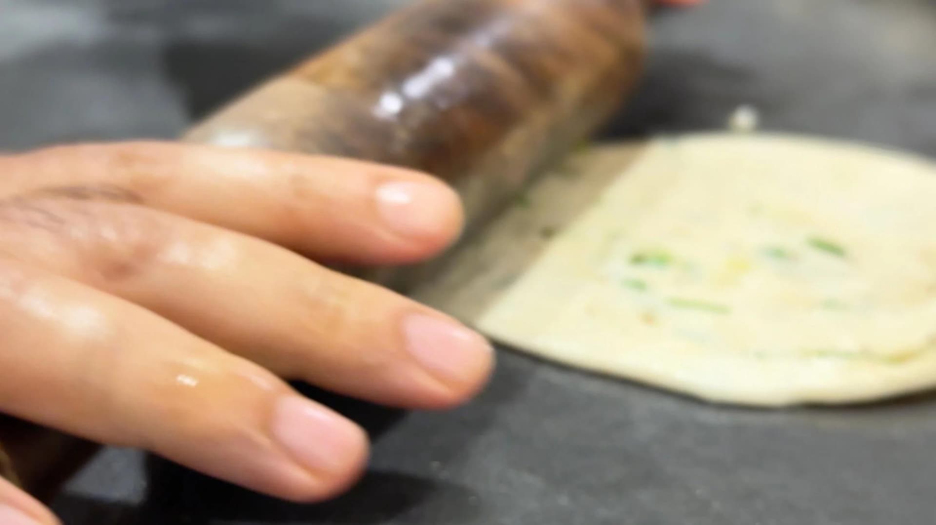 Hand flattening spiral dough into a thin disk with a rolling pin for scallion pancakes.