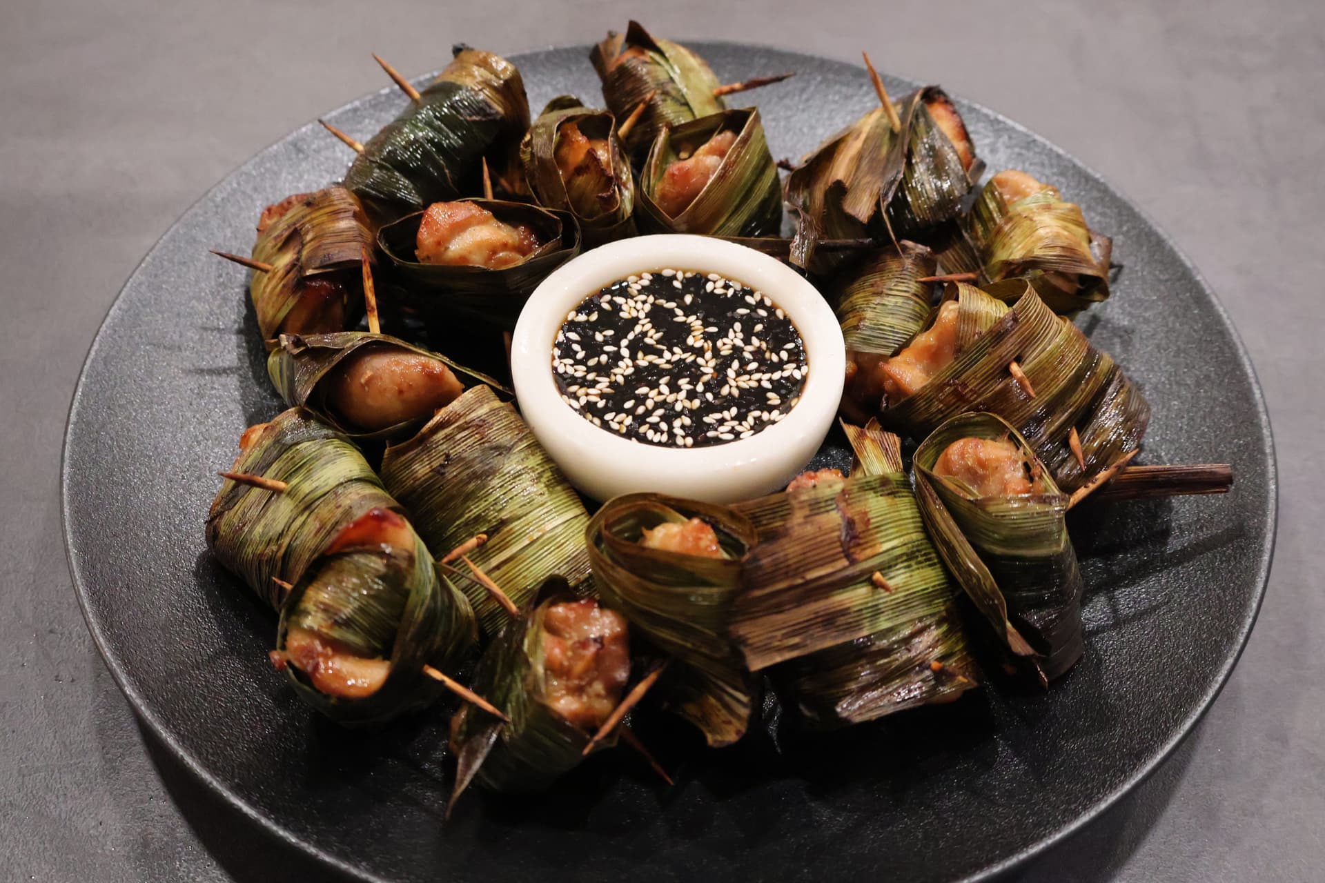 Crispy air fryer Thai pandan chicken parcels arranged in a circle on a dark plate with sesame seed dipping sauce in the center.
