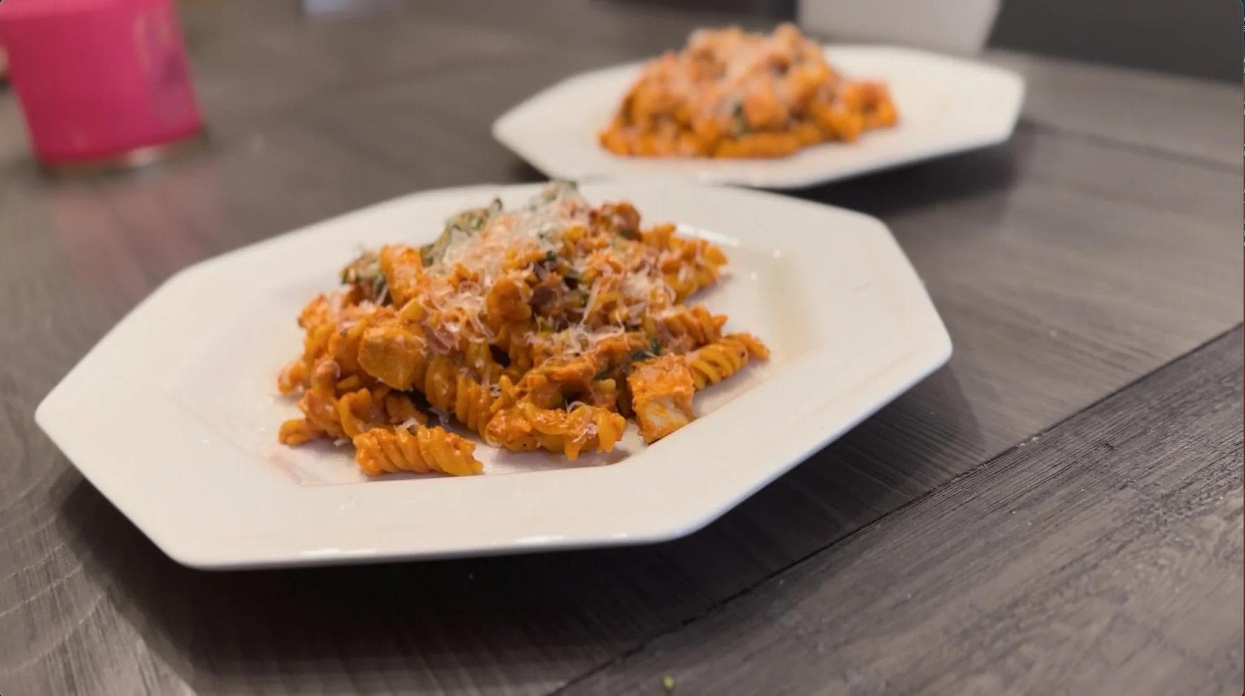 Creamy tomato chicken pasta with crispy wavy noodles topped with grated parmesan cheese, plated on white hexagonal dishes.