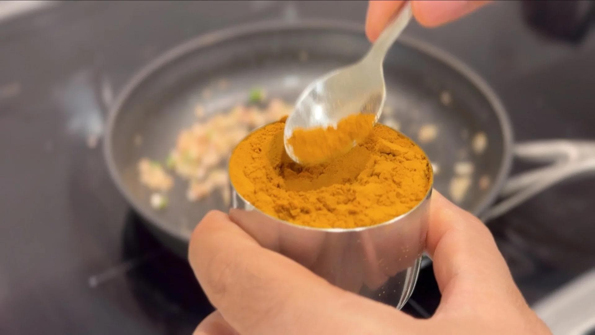 Adding turmeric powder to sautéed onions and spices in a pan for mushroom filling.