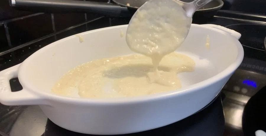 Béchamel sauce being poured into a white baking dish for lasagna assembly.