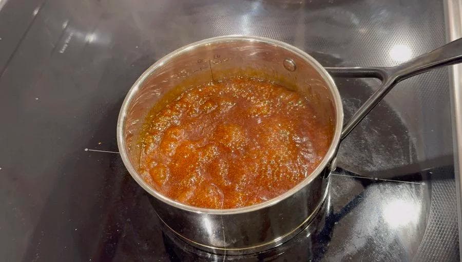 Homemade caramel sauce simmering in a saucepan on the stovetop with a rich amber color.