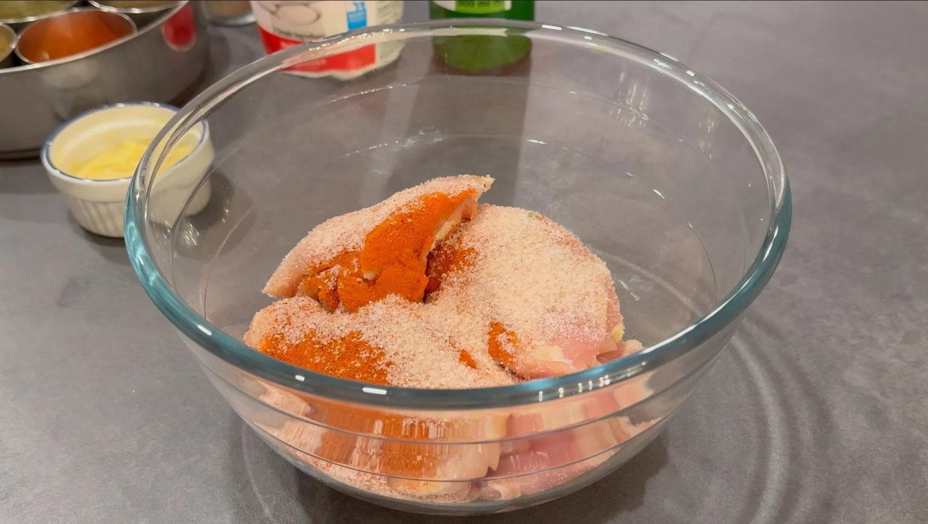 Raw chicken coated in spiced marinade in a glass bowl during first marinating stage.