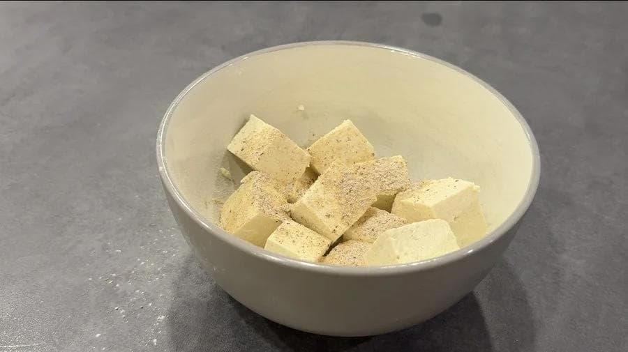 Cubed tofu seasoned with spices in a white bowl, ready for air frying.