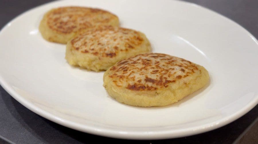 Three golden-brown llapingachos on a white plate, freshly sautéed until crispy.