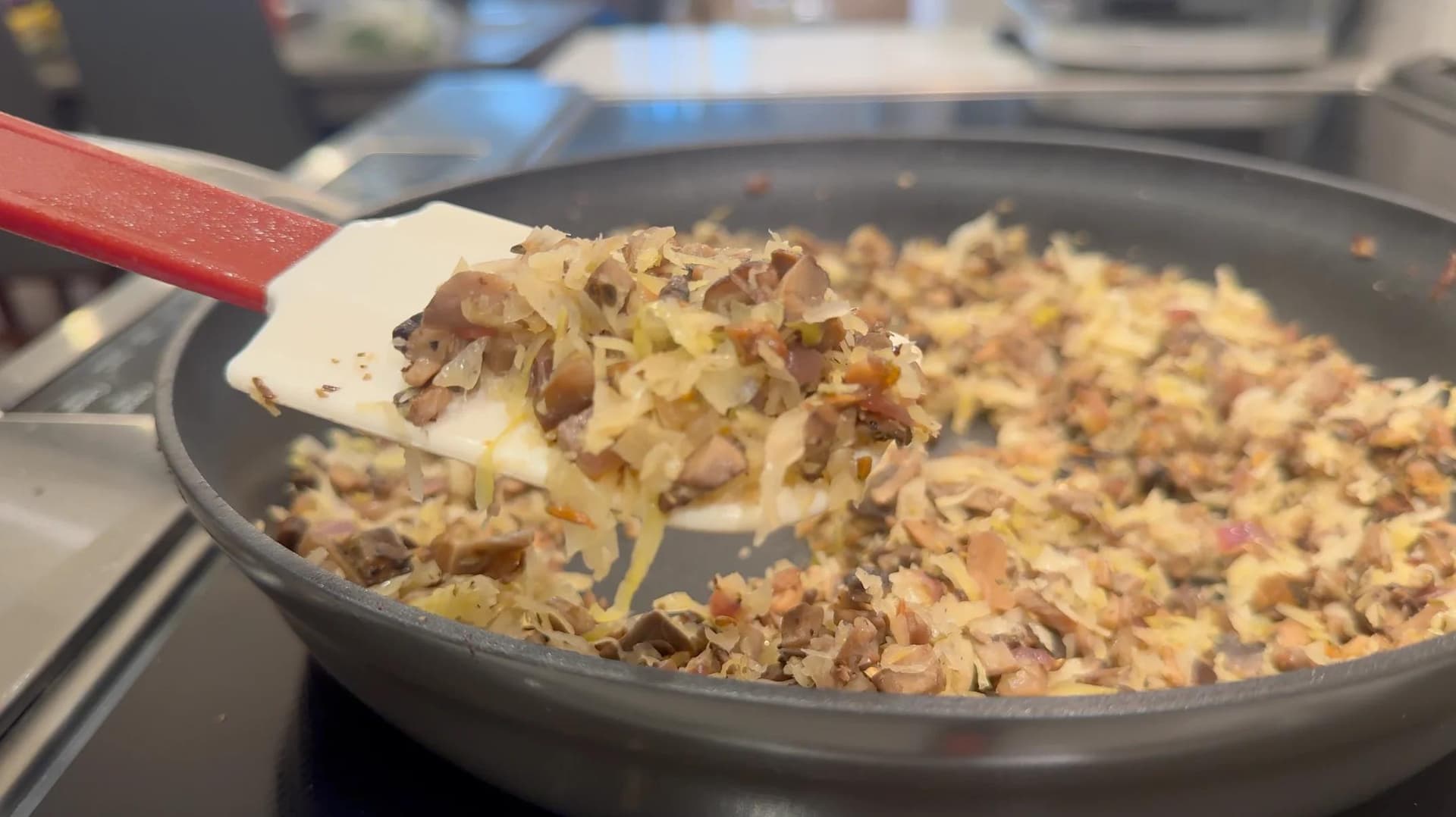 Spatula lifting cooked sauerkraut and mushroom mixture from pan, showing moist filling for Polish croquettes.
