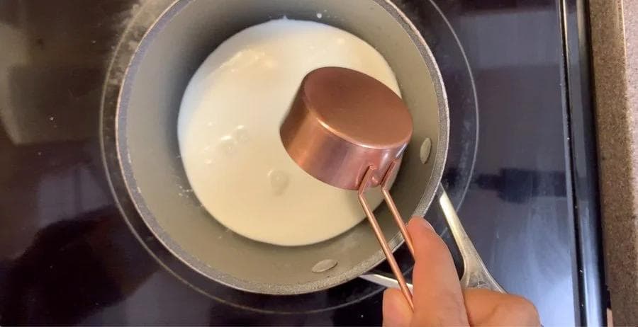 Pouring melted white chocolate into heavy cream in a saucepan during preparation of homemade white chocolate mocha.