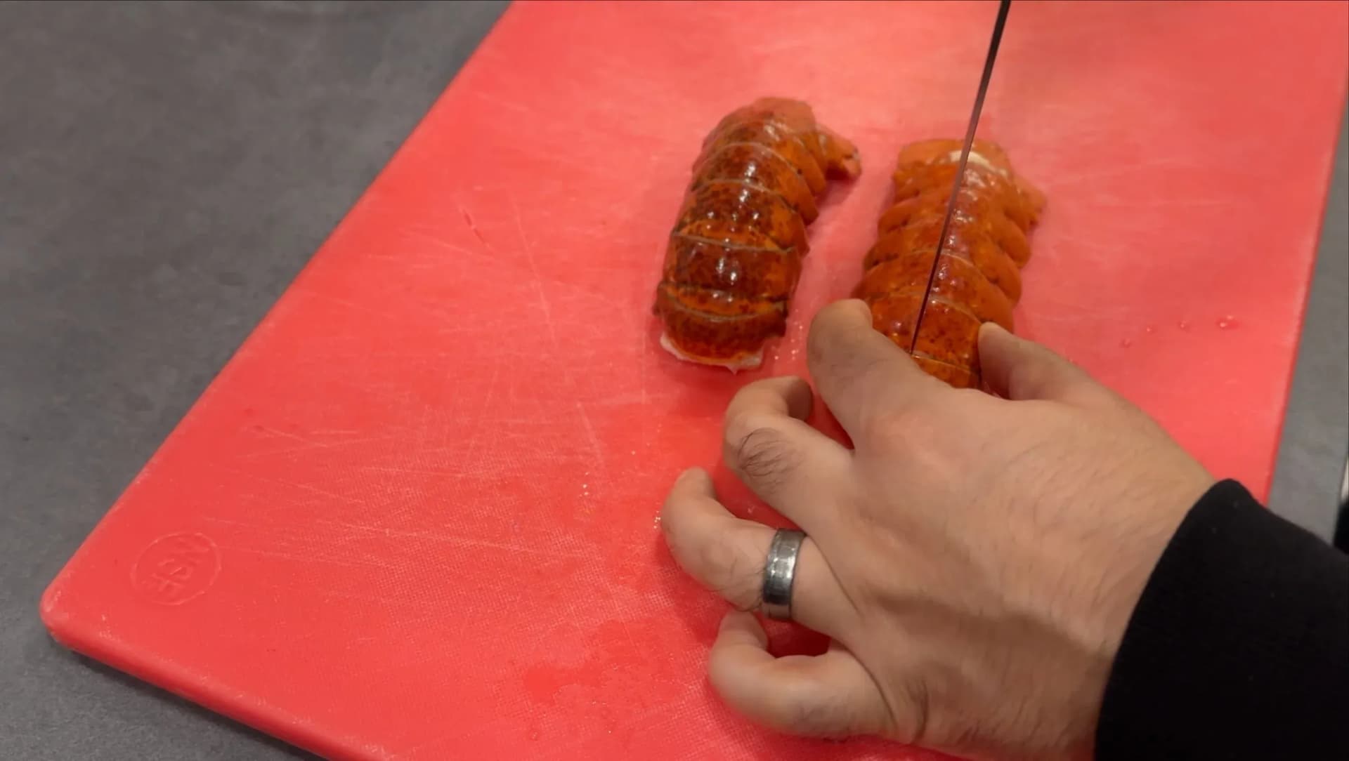 Hand removing cooked lobster meat from split tail shells on a red cutting board.