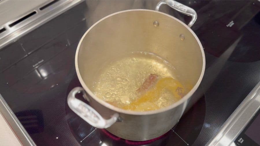 Pot of boiling water with cinnamon stick, star anise, ginger, and lemon peel for Arroz Con Leche.
