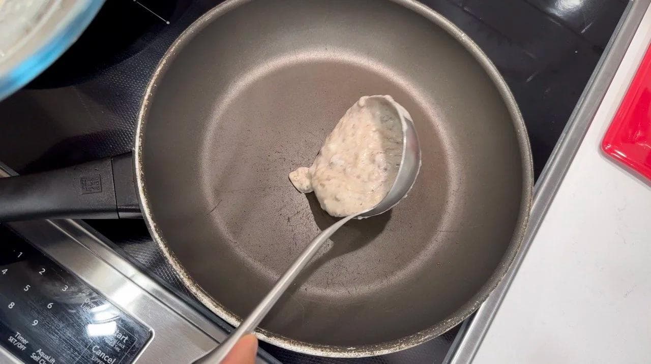 Pancake batter being poured from a ladle onto a hot non-stick skillet.