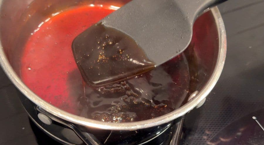 Red umami sauce simmering in a pot with a spatula stirring the thickened glaze coating the back.