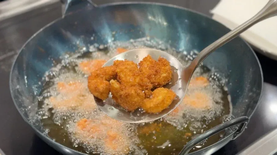 Golden-brown popcorn shrimp being removed from hot oil with a slotted spoon.