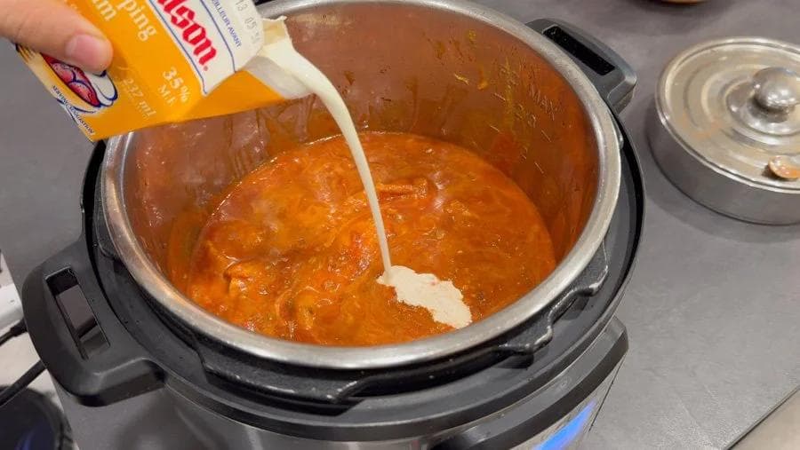 Heavy cream being poured into an Instant Pot of orange chicken tikka masala sauce.