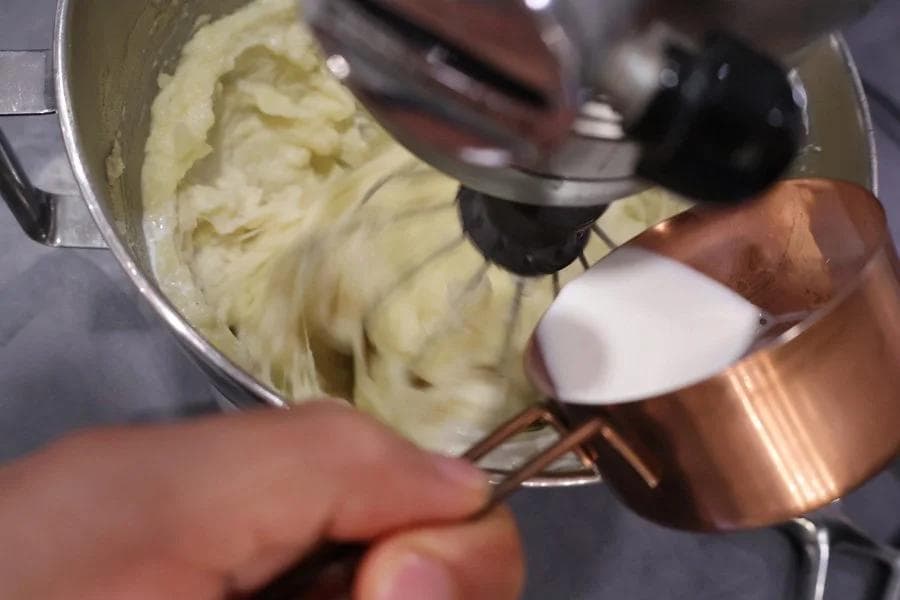 Hand mixer blending creamy mashed potatoes in a stainless steel bowl until smooth.