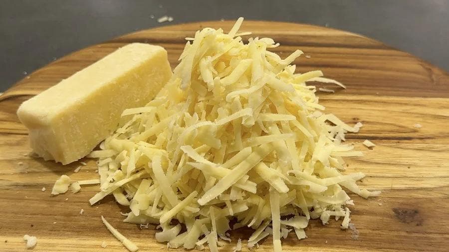 Block of cheddar cheese next to a pile of shredded cheddar on a wooden cutting board.