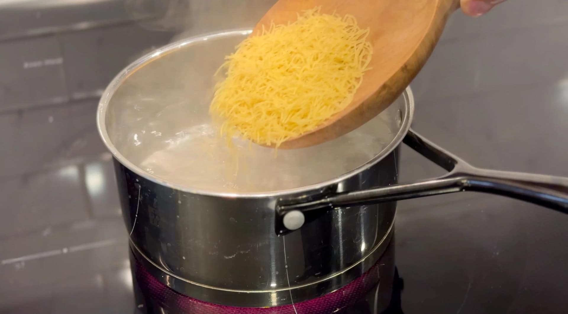 Pouring cooked yellow vermicelli into boiling water in a black saucepan.