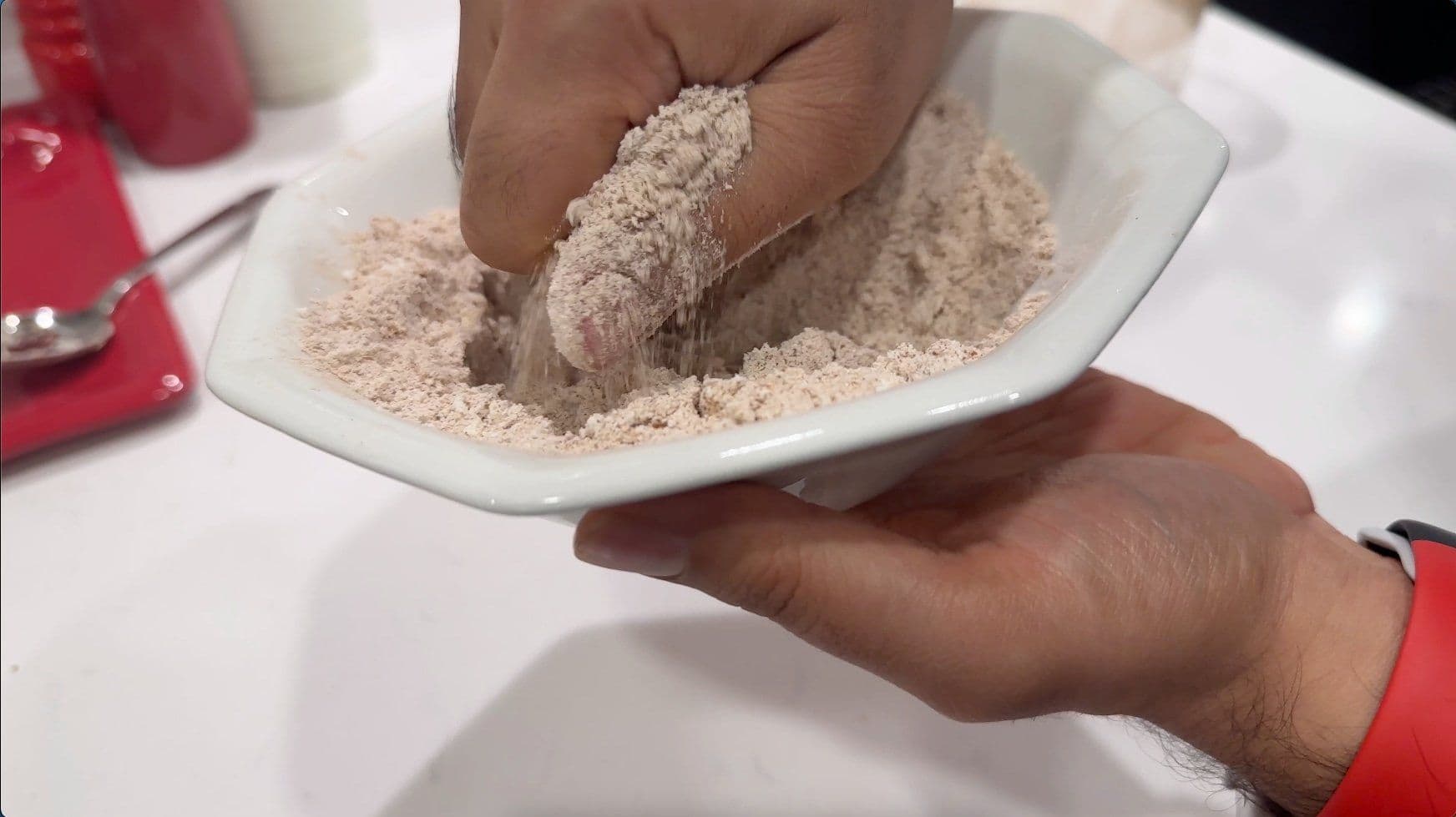 Hand holding white bowl of cinnamon sugar crumble mixture with pea-sized butter pieces visible.