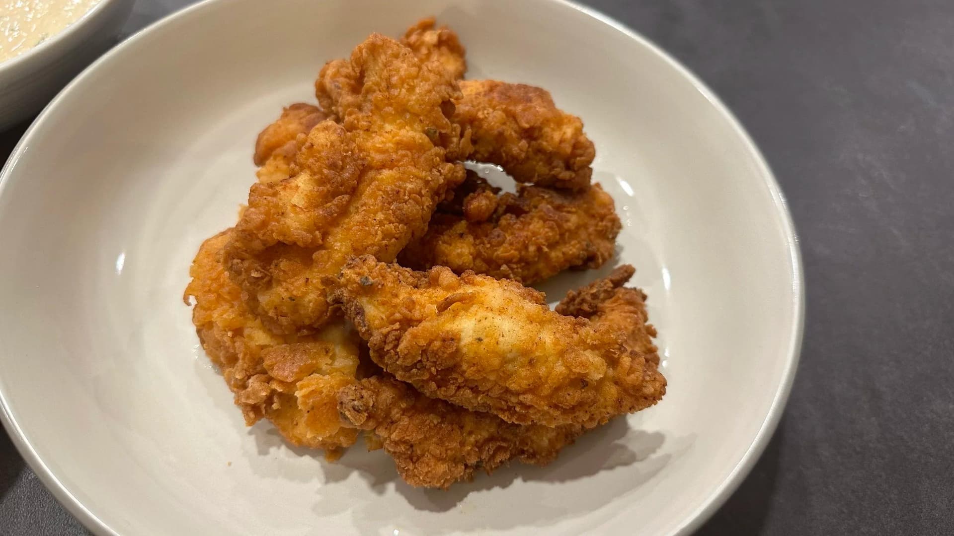 Golden-brown crispy fried chicken tenders piled on a white plate, showing the breaded coating and cooked exterior.