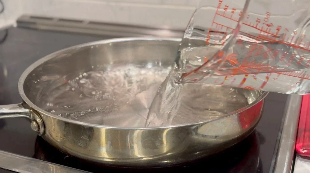 Water being poured into a stainless steel pan with steaming momos inside during cooking.