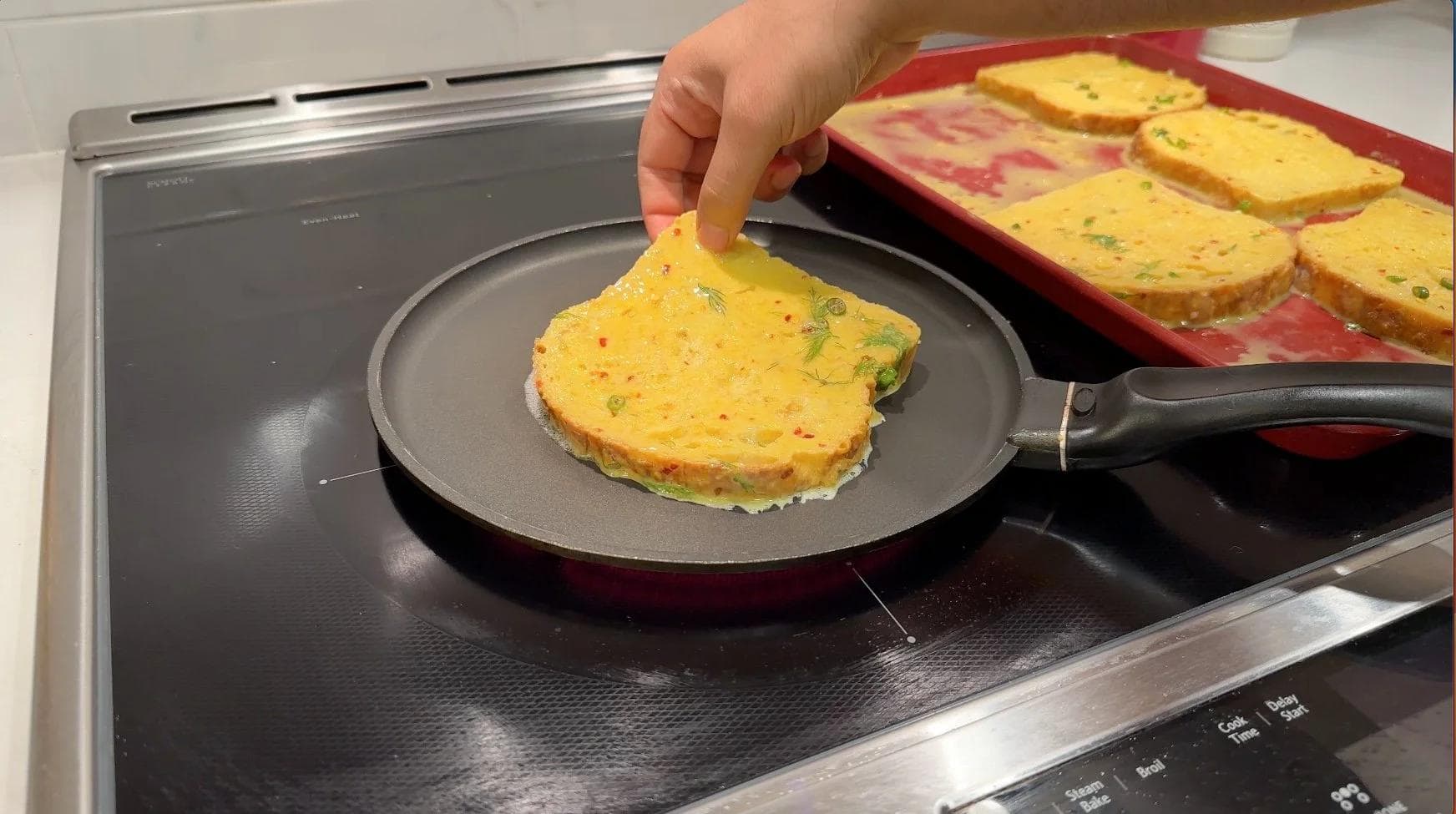 Hand placing savory Indian-spiced French toast onto a nonstick pan with melted butter on a stovetop.
