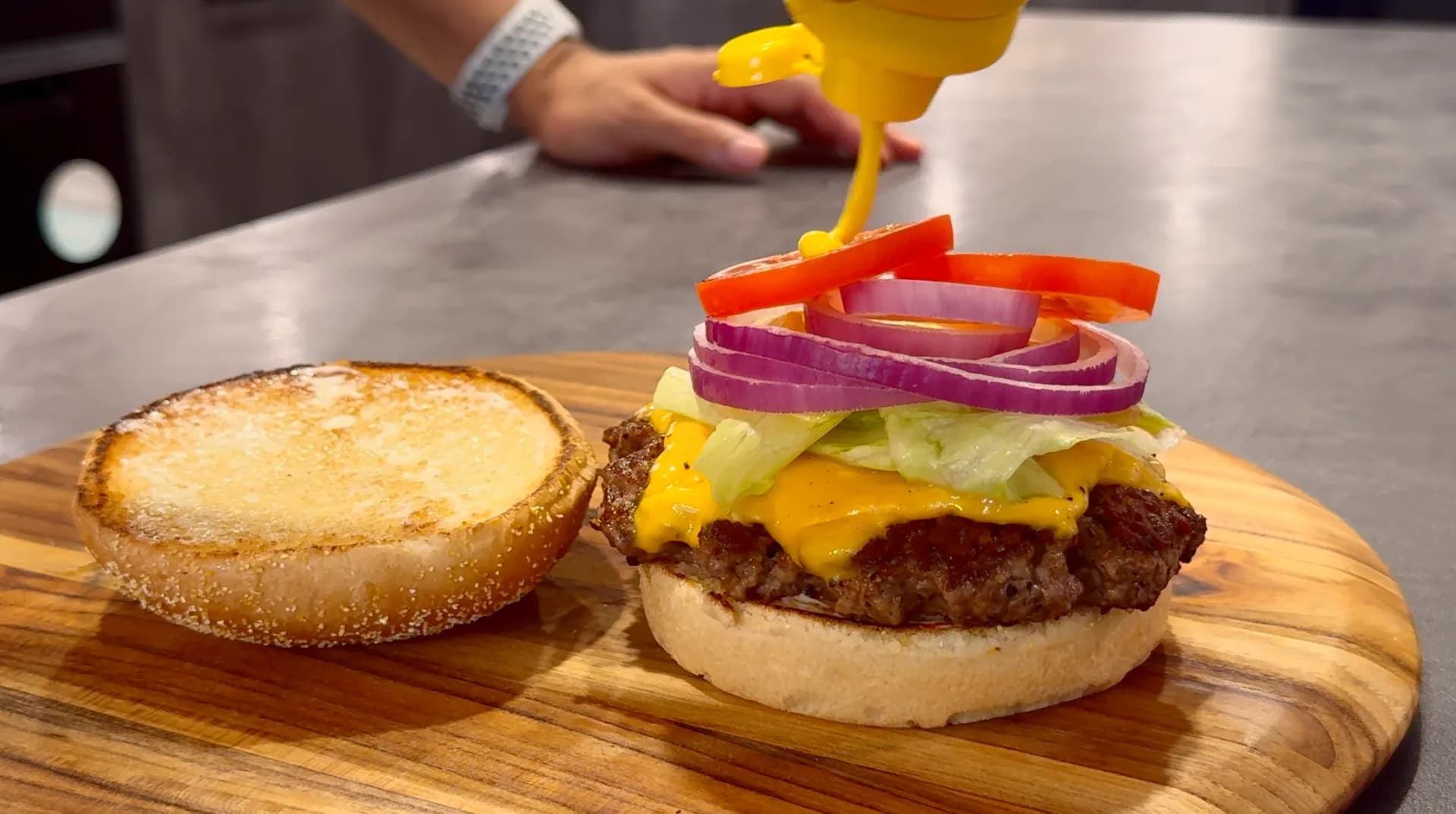Classic cheeseburger with melted yellow cheese, fresh lettuce, red onion, and sesame seed bun, served with a toasted bun side.