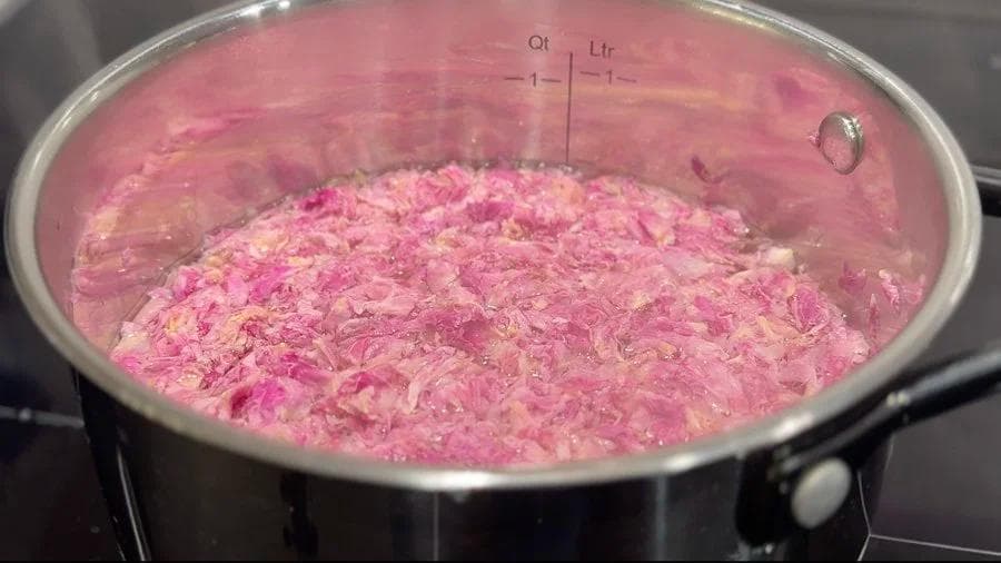 Rose petals simmering in water in a saucepan, turning the liquid pink for gulabi doodh.